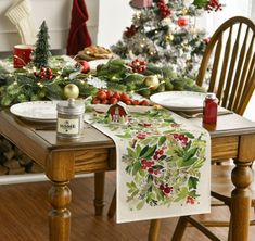 the table is set for christmas dinner with holly and berries on it, along with other holiday decorations