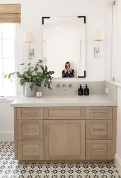 a woman taking a selfie in the mirror above a bathroom vanity with wooden cabinets and drawers