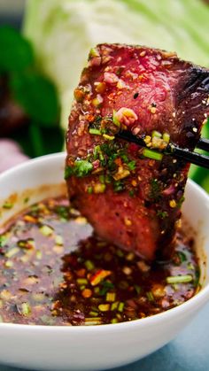 the meat is being lifted from the bowl with chopsticks