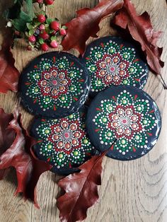 three black painted rocks sitting on top of a wooden table next to leaves and flowers