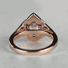 a rose gold ring with a white diamond in the center on a gray surface,