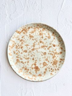 a white plate with brown speckles sitting on a white tablecloth covered wall