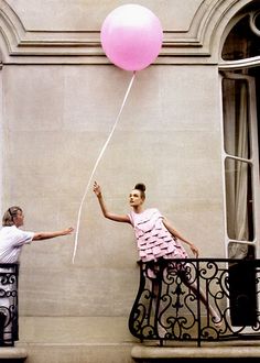 a woman standing on a balcony with a pink balloon in her hand and the word g is written below it