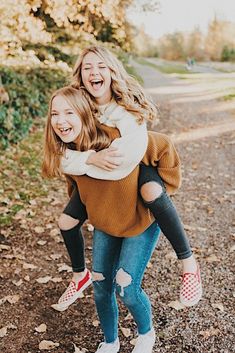 two girls laughing and hugging each other in the park with autumn leaves on the ground