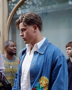 a man in a denim jacket and white shirt is standing with other men behind him