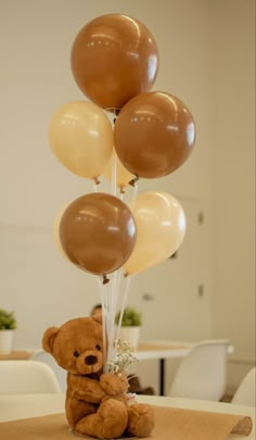 a teddy bear sitting on top of a table with balloons in the shape of animals