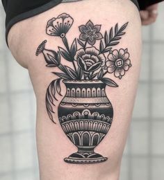 a black and white vase with flowers in it on the thigh by tattoo artist mark