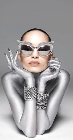 a woman in silver is posing with her hands behind her head and wearing sunglasses on top of her head