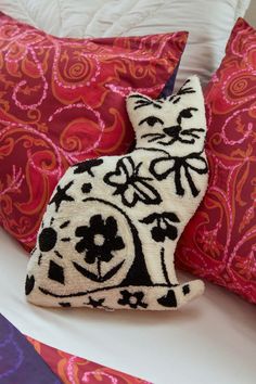 a cat pillow on top of a bed with red and purple pillows in the background