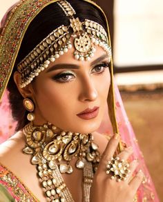 a woman in a bridal outfit with jewelry on her neck and hands near her face