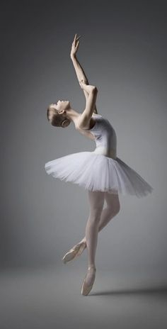 a ballerina in white tutu is posing for the camera on a gray background