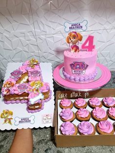 a pink cake and cupcakes are sitting on the table next to each other