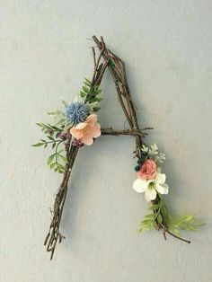 a letter made out of twigs with flowers and leaves on it's sides, hanging from the wall