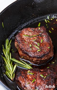 two steaks cooking in a skillet with green onions and rosemary sprigs