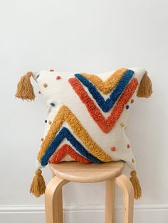 a colorful pillow with tassels on it sitting on a wooden stool