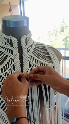 a woman is working on a piece of white crocheted material with scissors and yarn