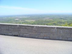 a stone wall on the side of a road overlooking a valley and mountains in the distance