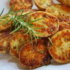 some potato wedges are on a plate with rosemary sprigs and seasoning