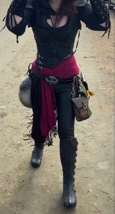 a woman dressed in black and red walking down a dirt road