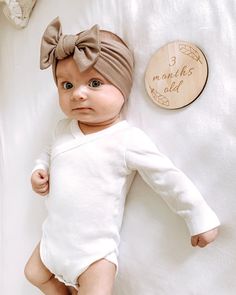 a baby doll laying on top of a bed next to a wooden plaque that reads 3 months old