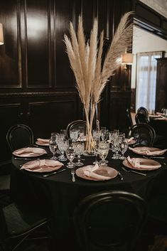 the table is set with plates, silverware and tall pamphini reeds