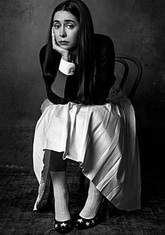 a black and white photo of a woman sitting in a chair with her hand on her chin