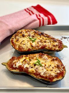 two stuffed eggplant halves on a baking sheet with a red towel and napkin in the background