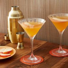 two glasses filled with drinks sitting on top of a table next to an apple slice