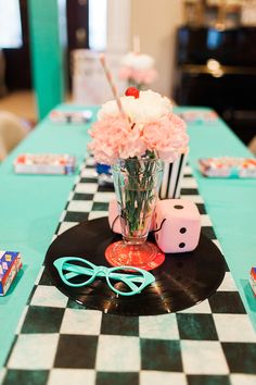 a table topped with a vase filled with flowers next to dice and pink carnations