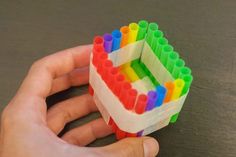 a hand holding a small building made out of colored legos on top of a table