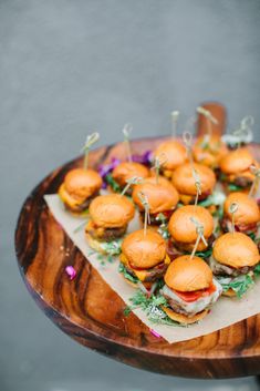 mini burgers are arranged on napkins on a wooden platter with green sprigs