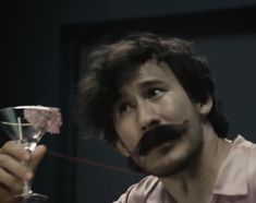 a man with a moustache on his face holding a wine glass in front of him