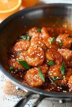 a pan filled with shrimp and sauce on top of a table next to an orange