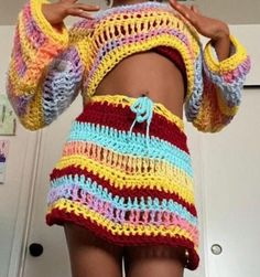 a woman wearing a colorful crochet skirt and matching sweater is looking at her cell phone