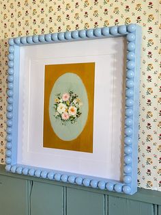 a blue frame with flowers is hanging on the wall