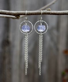 These earrings feature faceted nuggets of lavender quartz framed by a diamond cut, silver ring. A tassel of sterling silver chains dangle from below. These long drops measure 16.5mm in width and hang 70mm in length from sterling silver, ear wires.  Also known as lavender moon quartz, this stone is a very rare form of quartz that is only mined in Boquira, Brazil. What makes this stone rare is its color, since quartz rarely appears with this light tint of purple naturally. It contains manganese and titanium, which classifies it as a type of rose quartz. Metaphysically, it promotes general healing and self-love. It can also help relieve feelings of loneliness, isolation, and anxiety. Long Earring Crystal Ametyst, Silver Amethyst Drop Crystal Earrings, Silver Amethyst Dangle Earrings, Mixed Metal Amethyst Square Dangle Earrings, Spiritual Amethyst Drop Earrings, Small Drop Earrings, Lavender Quartz, Spike Earrings, Long Drop Earrings