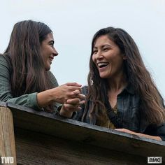 two women are smiling and looking at each other while sitting in a wooden box on top of a building