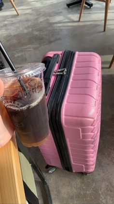 a person holding a drink next to a pink piece of luggage