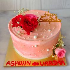 there is a pink cake with red flowers on the top and gold lettering that says ashwinwarsha