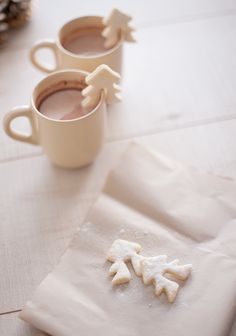 two cups of hot chocolate on top of a white napkin next to some small snowflakes