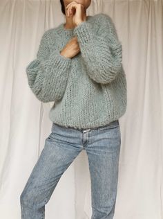 a woman is posing in front of a white curtain wearing jeans and a green sweater