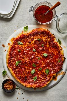 a pizza sitting on top of a white plate next to a bowl of sauce and pepperoni