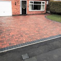 a brick driveway in front of a house with two garage doors on the other side