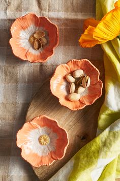 three orange flowers sitting on top of a wooden cutting board