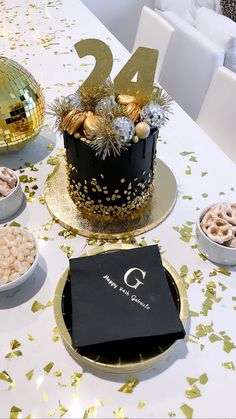 a table topped with a black cake covered in gold confetti next to other desserts