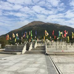 many flags are flying in the air near some steps and buildings with mountains in the background