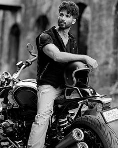 black and white photograph of a man sitting on a motorbike in front of an old building