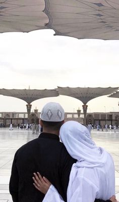 a man and woman hugging in front of an open area with many umbrellas overhead