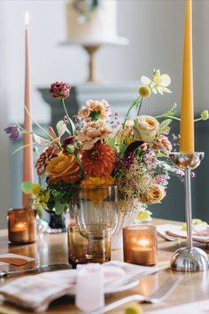 an arrangement of flowers and candles on a table