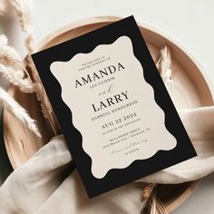 a black and white wedding card on top of a plate with some feathers in the background